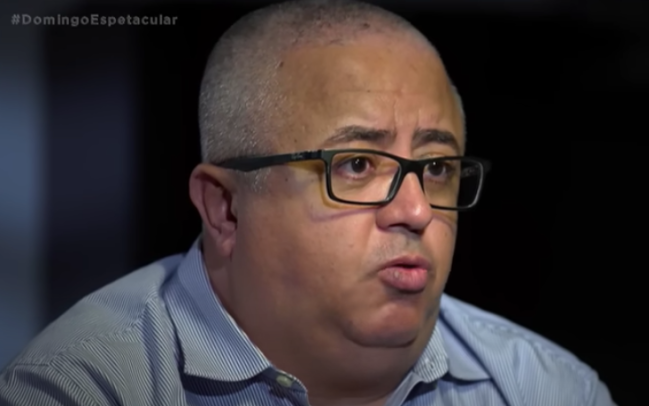 Ricardo Rocha um homem branco de óculos de grau falando e um fundo escuro atrás
