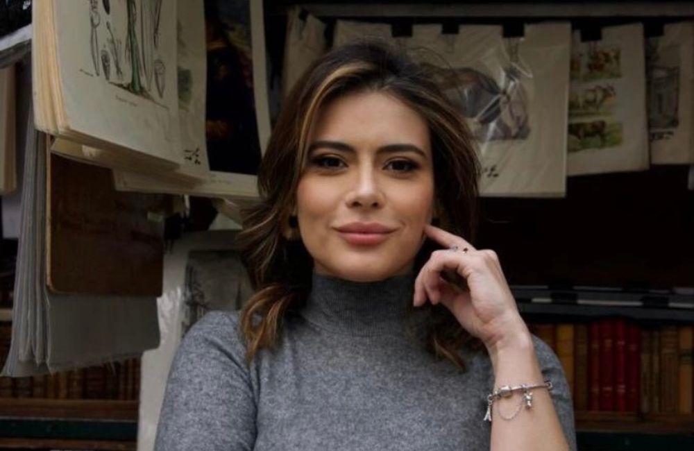 Michelle Loreto usando um vestido cinza e sorrindo