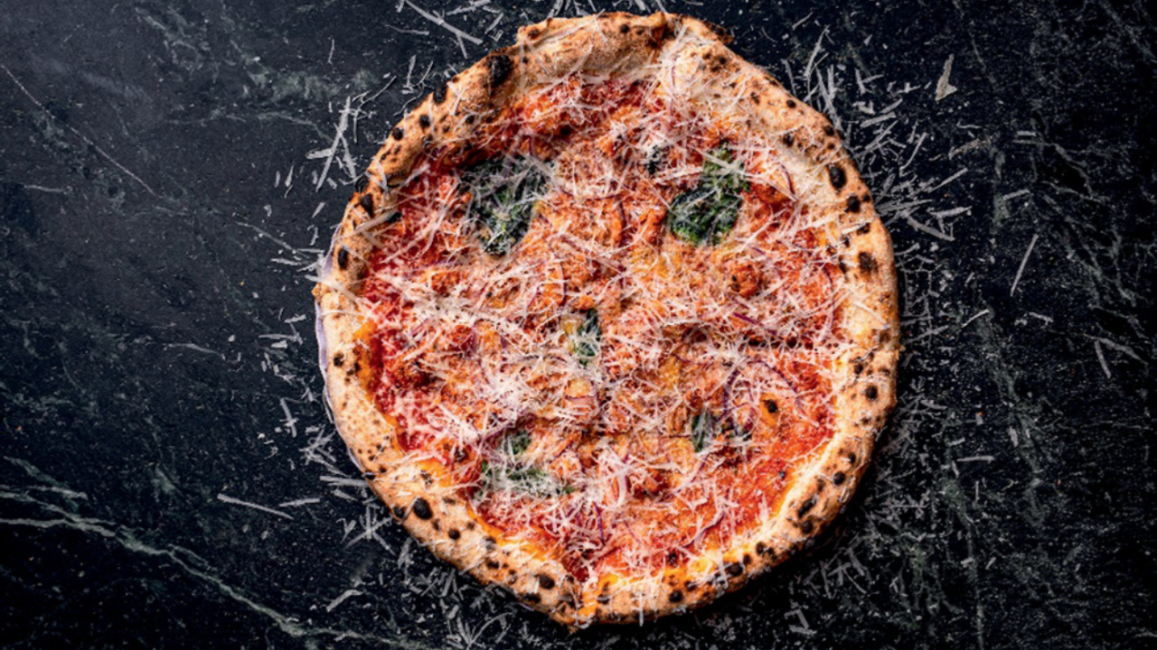 Pizza sobre tampo de mármore com molho de tomate e queijo ralado por cima.