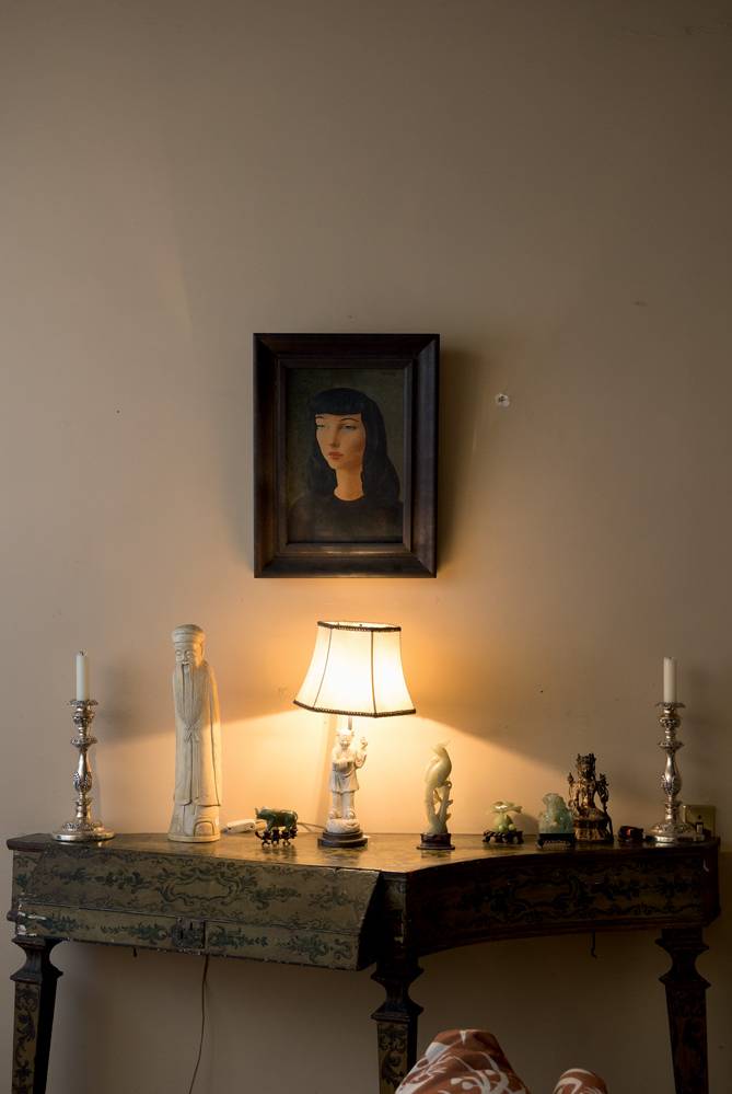 Leilão Familia Prado – Quadro Moïse Kisling (Wanezza Soares-Veja SP) (10) Parede com quadro de retrato de uma moça de cabelos pretos e mesa de canto com peças de marfim.