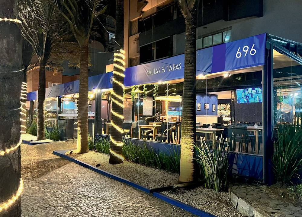 Fachada azul do bar Saltas & Tapas com coqueiros na frente.