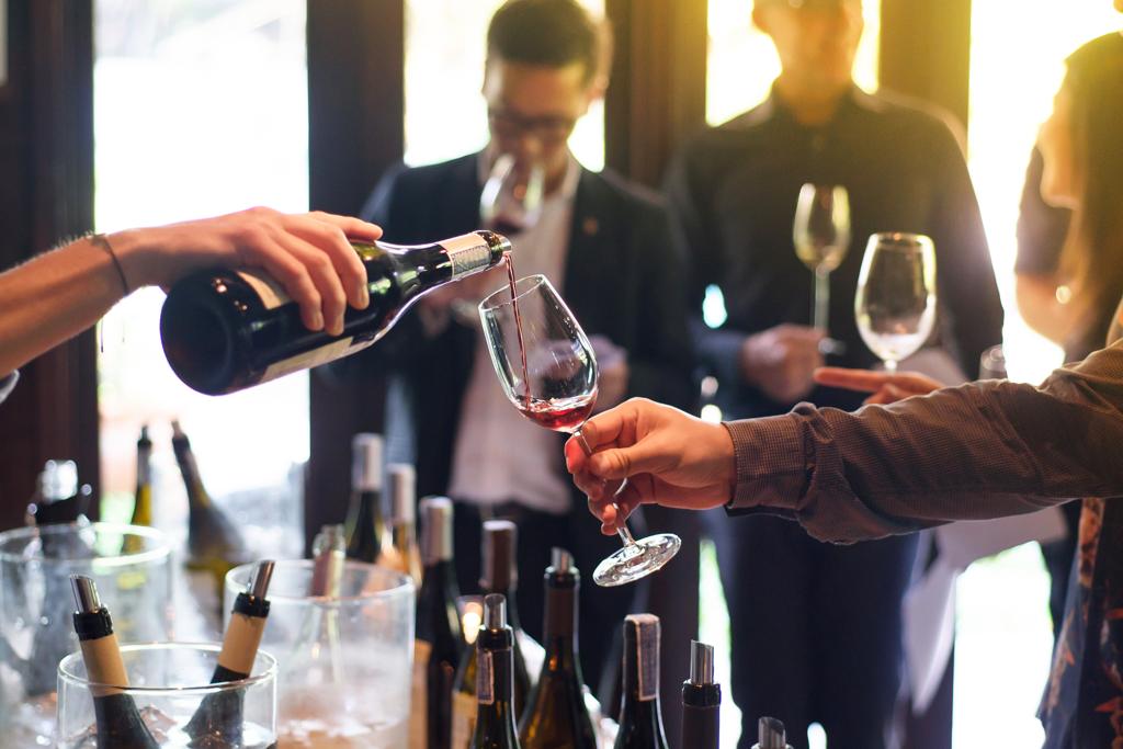 Feira de vinhos com mão segurando taça sendo servido de tinto.