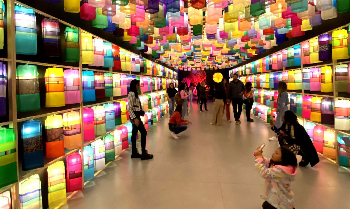 um corredor cheio de pessoas posando em frente à lanternas de cores variadas