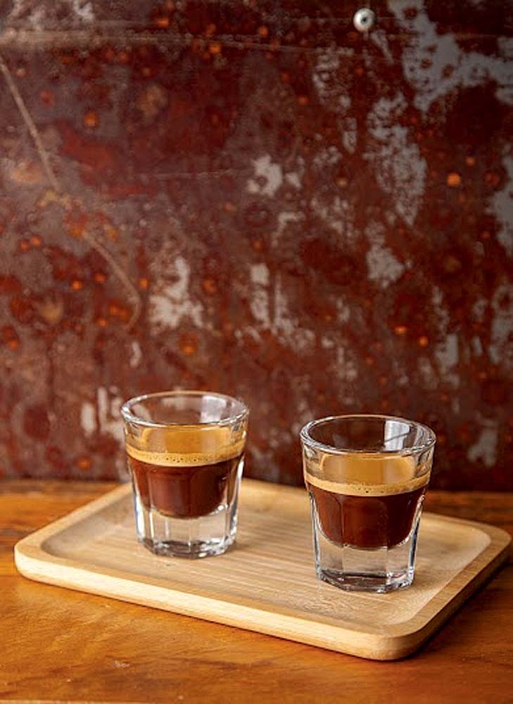 Fora da Lei Café Dois copinhos de vidro com café expresso dentro em bandeja de madeira.