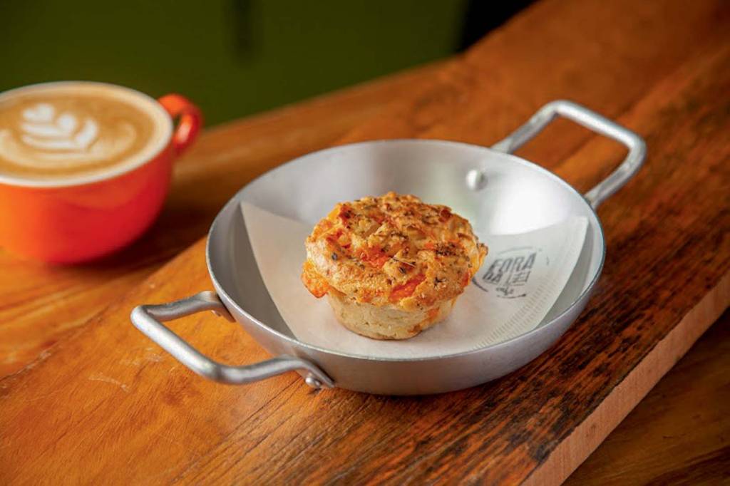 Fora da Lei Café Panelinha de metal sobre superfície de madeira com muffin de legumes ao centro.