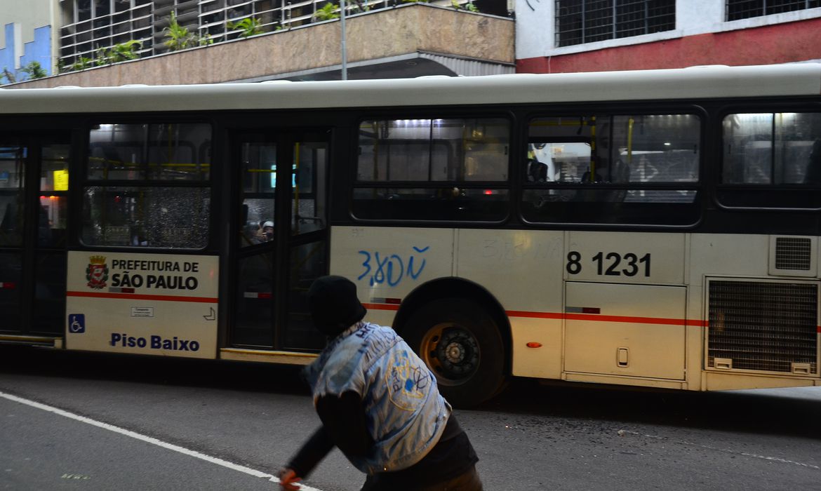uma pessoa de capuz jogando pedra em um ônibus