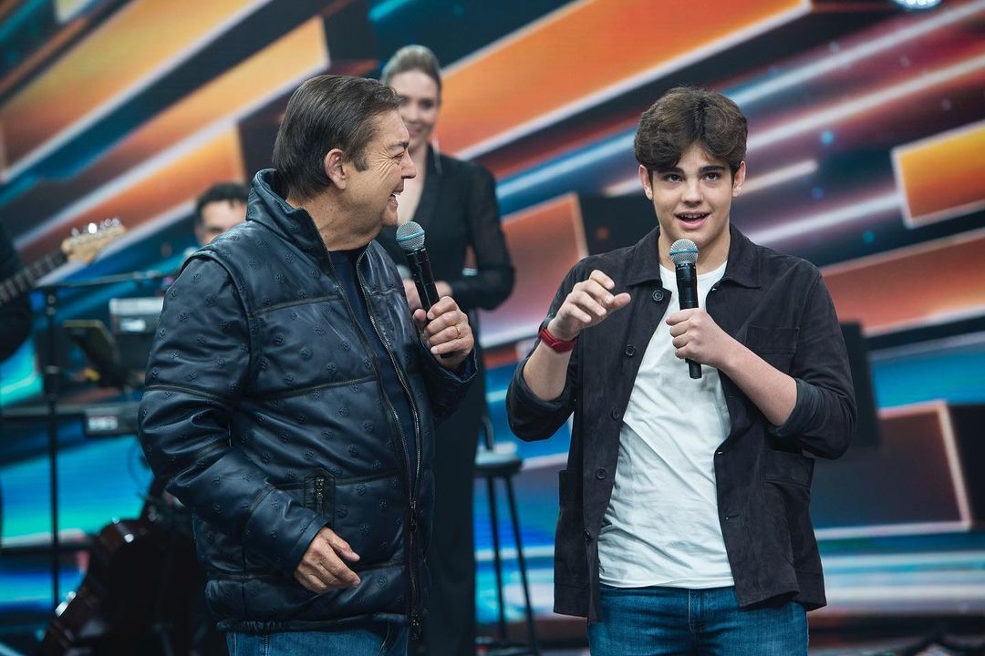 um homem branco ao lado de um jovem branco no palco do programa