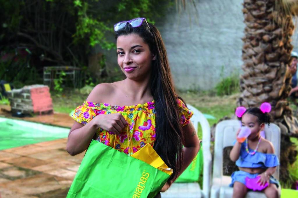 Moça negra posa com óculos na cabeça e vestido verde com estampa tropical.