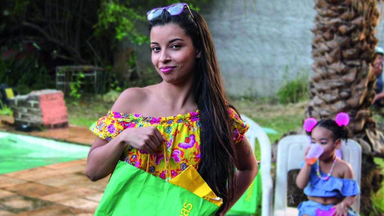 Moça negra posa com óculos na cabeça e vestido verde com estampa tropical.