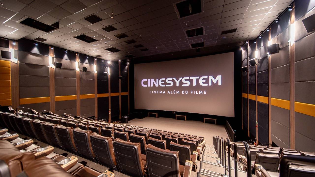 Sala de cinema com poltronas e telão ao fundo.