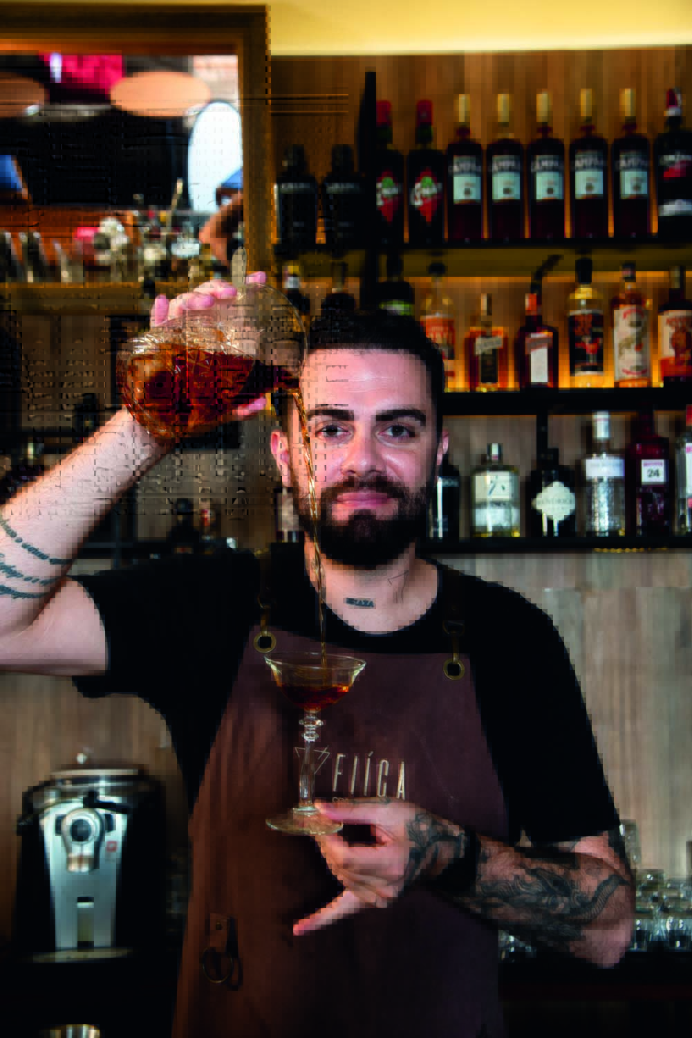 Fiíca Bar Bartender atrás de balão derrubando drinque de coqueteleira em taça.