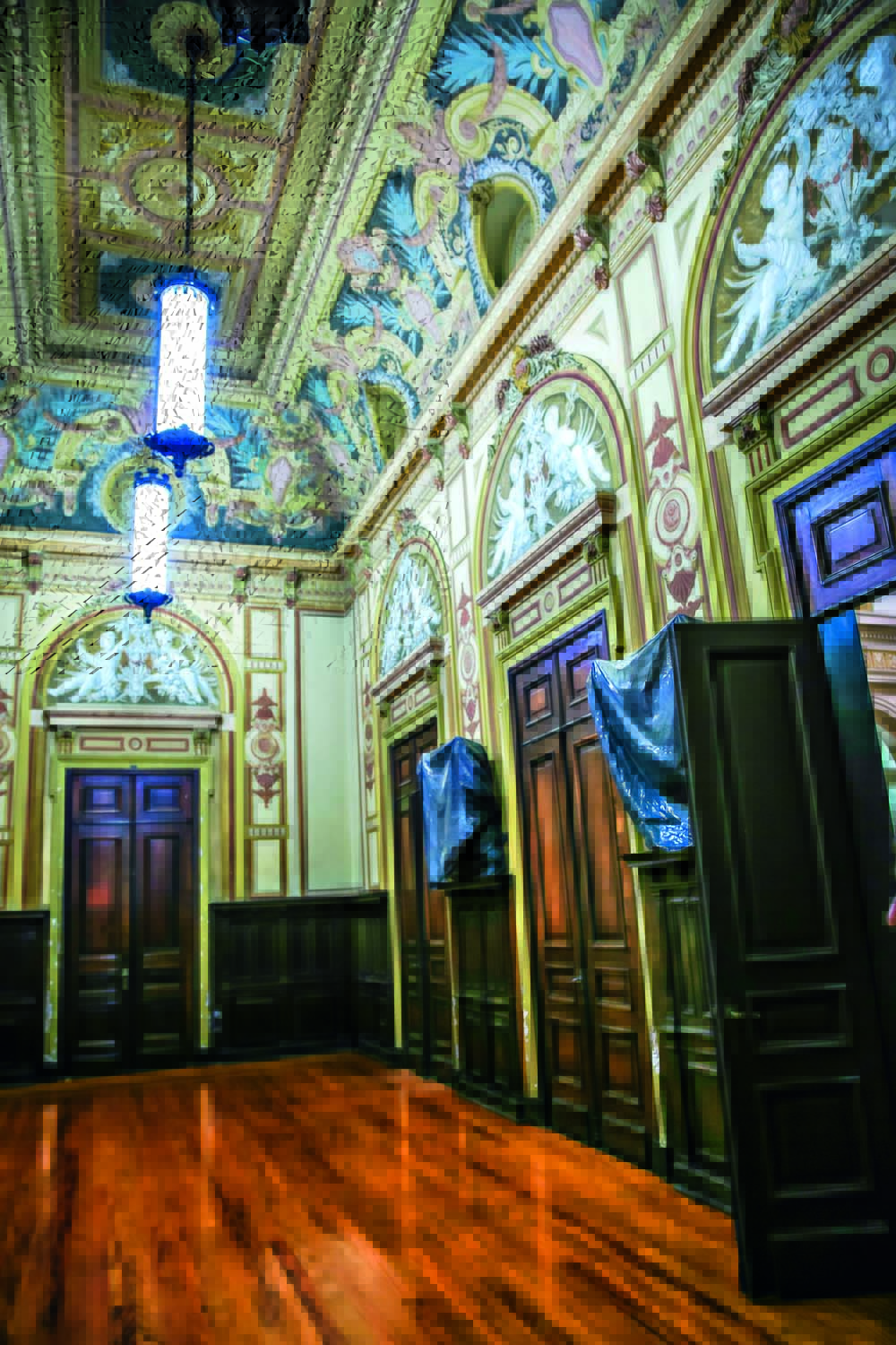 SALADOSANJOS_SECJUSTICA_1.JPG Sala com afrescos no topo e várias entradas com portas escuras. Dois lustres individuais aparecem pendurados.