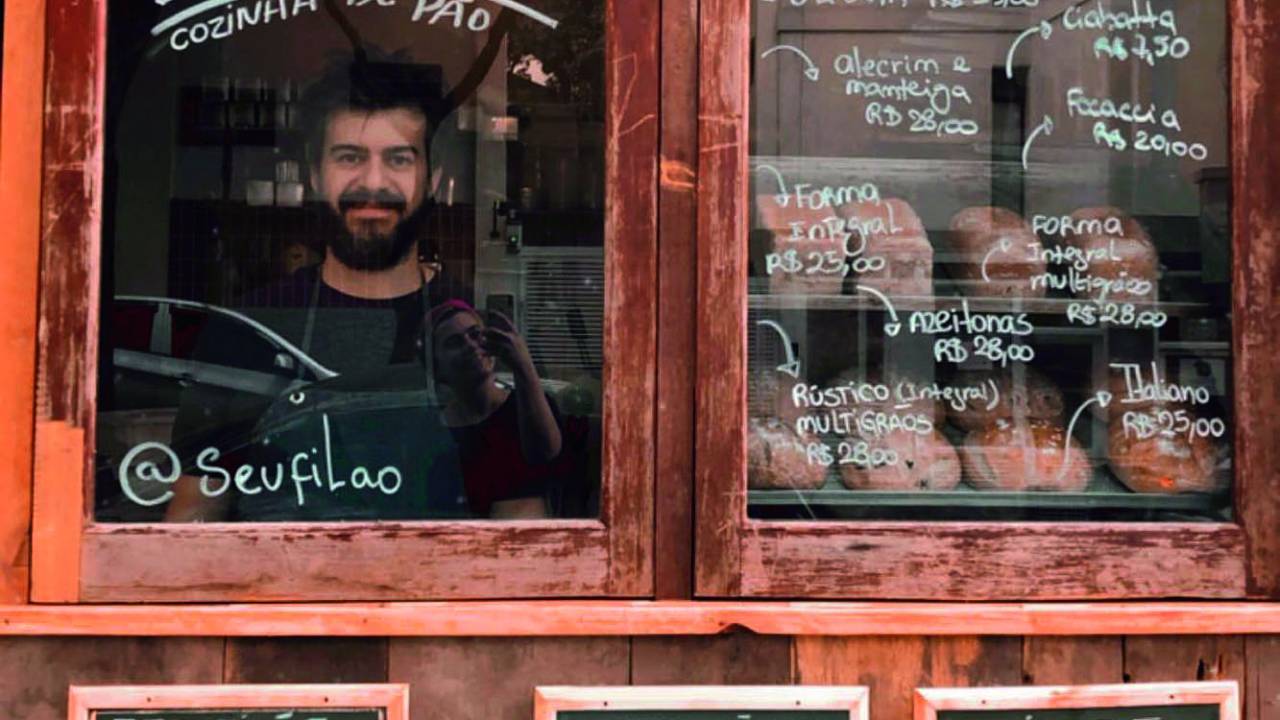Fachada de madeira com vidro da padaria Seu Filão com escritos em giz no vidro e em pequenas lousas abaixo.
