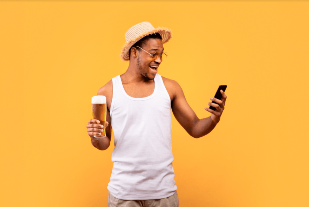 Homem segurando um copo de cerveja em uma mão e um celular na outra
