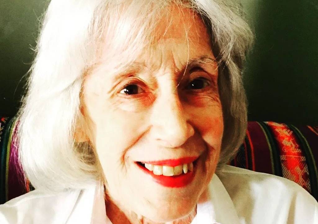 uma senhora branca de cabelos grisalhos sorrindo para a câmera