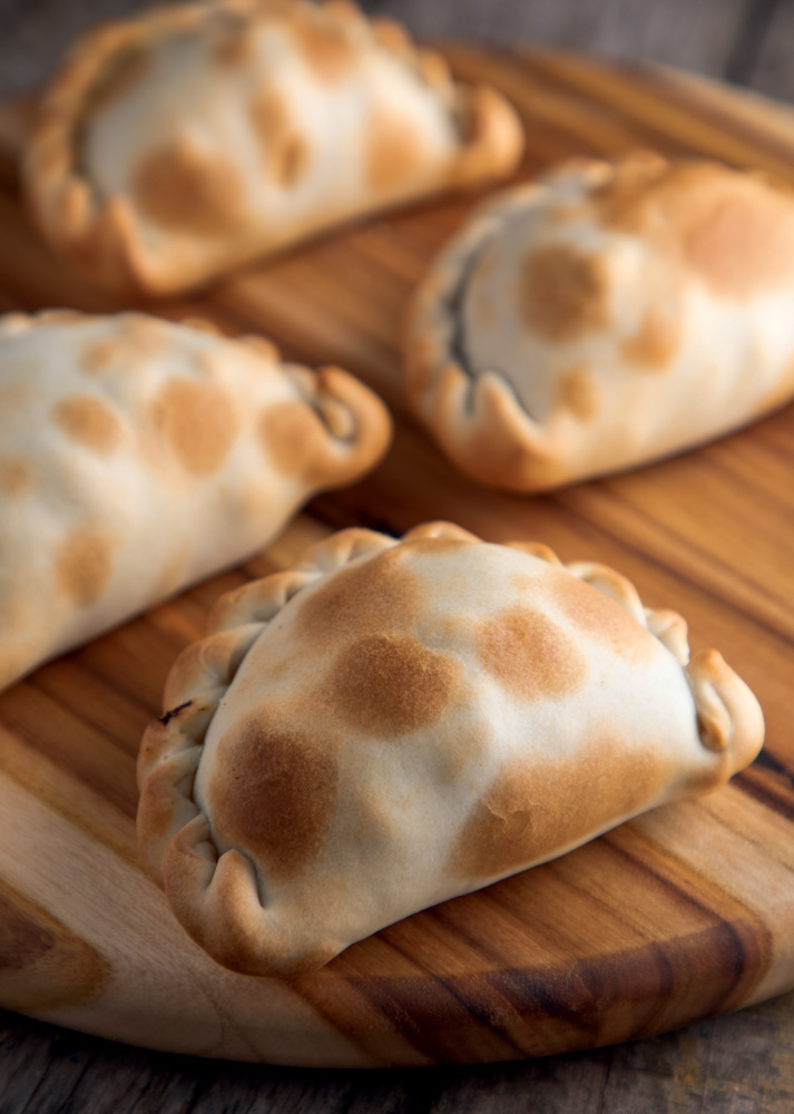 empanada do chef _ Rotiseria Argentina _ comidinhas A imagem mostra várias empanadas sobre uma mesa de madeira.