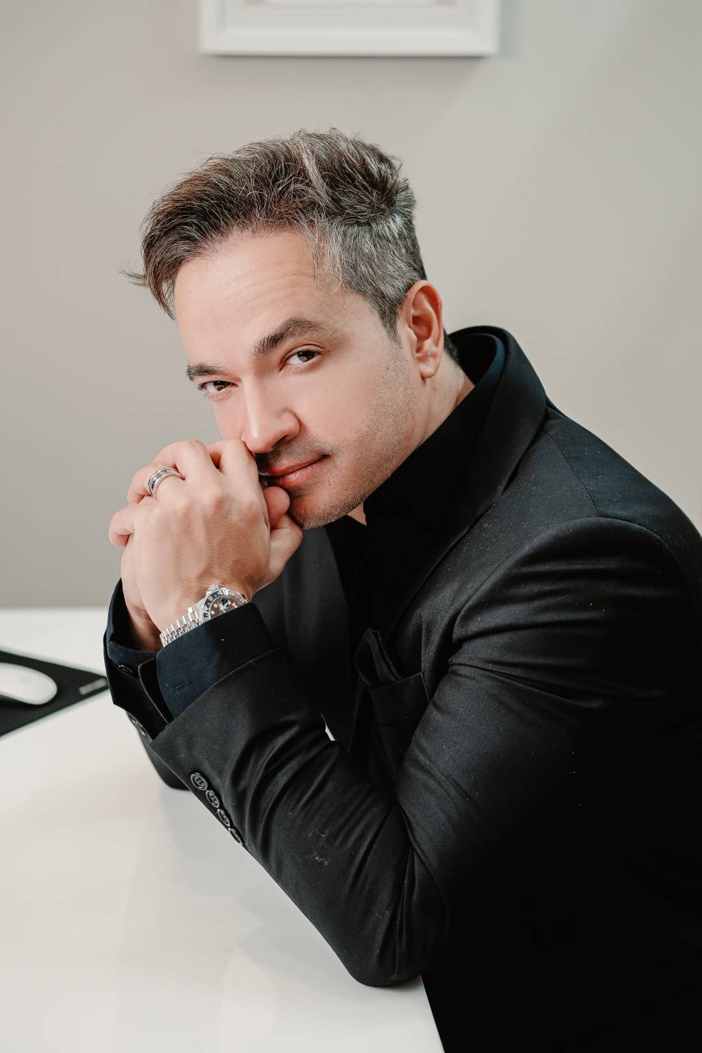 Ícaro Samuel (Glauber Matos-Divulgação) Homem jovem grisalho posa de lado com as mãos próximas ao queixo. Ele encara a câmera e veste blazer preto.