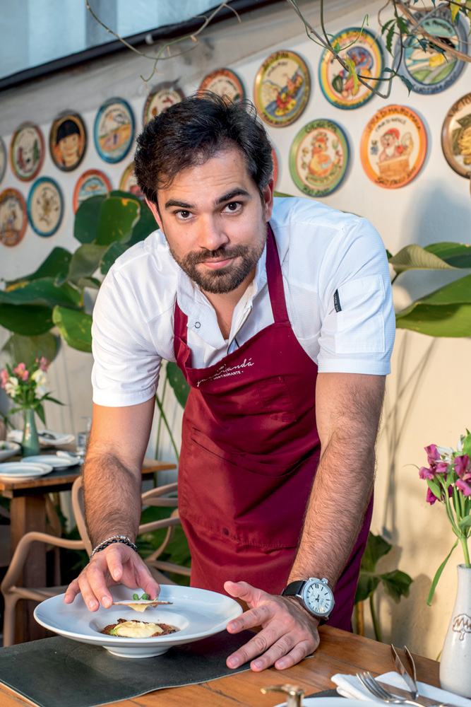 Jacarandá Chef de cozinha de avental vinho finalizando prato na mesa enquanto olha para a foto