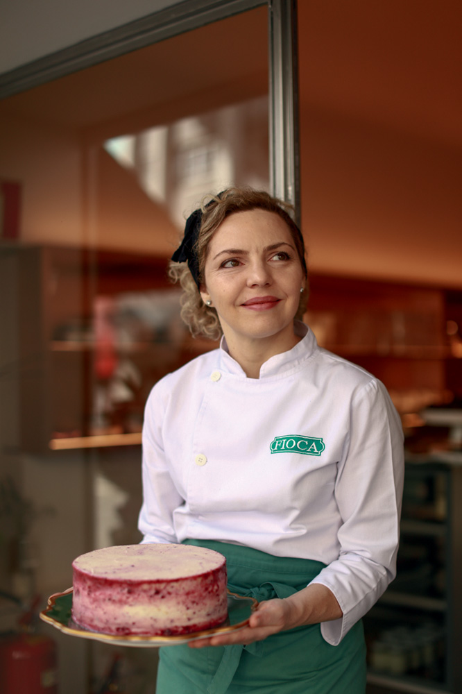 Mulher de dólmã e avental segurando bolo.