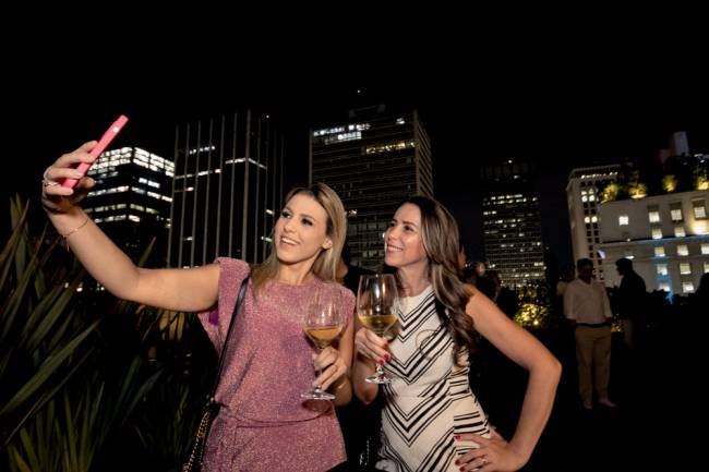 Imagem mostra duas mulheres com taça nas mão tirando selfie