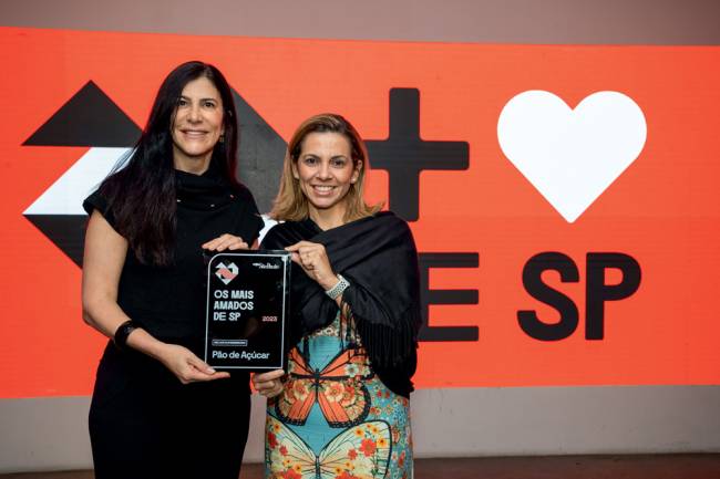 Imagem mostra duas mulheres segurando placa com o nome do Pão de Açúcar na frente de telão da premiação