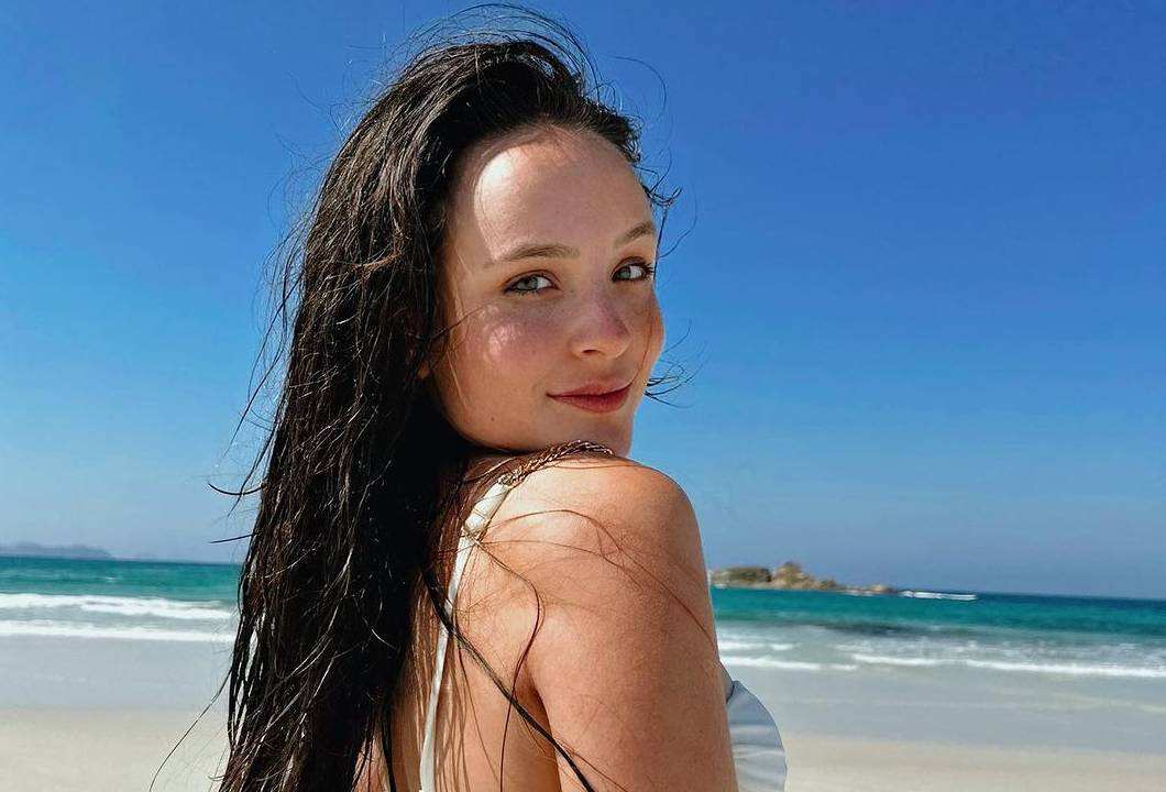 uma mulher branca de biquini e cabelos molhados na praia