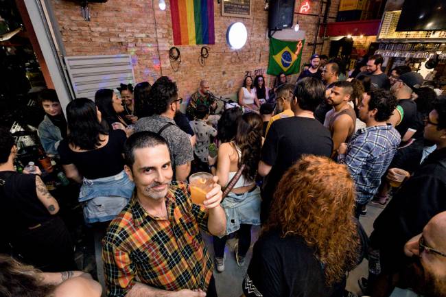 sirigoela Daniel olha para a foto segurando um drinque em ambiente lotado com roda de samba ao fundo