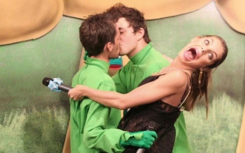 Beija Sapo (MTV Brasil-Reprodução) Imagem exibe dois homens de verde se beijando e apresentadora com cara de surpresa no meio.