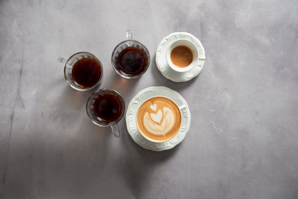 COMER & BEBER 2023 – Coffee Lab Diversas xícaras de café e cappuccino vistas de cima em fundo cinza.