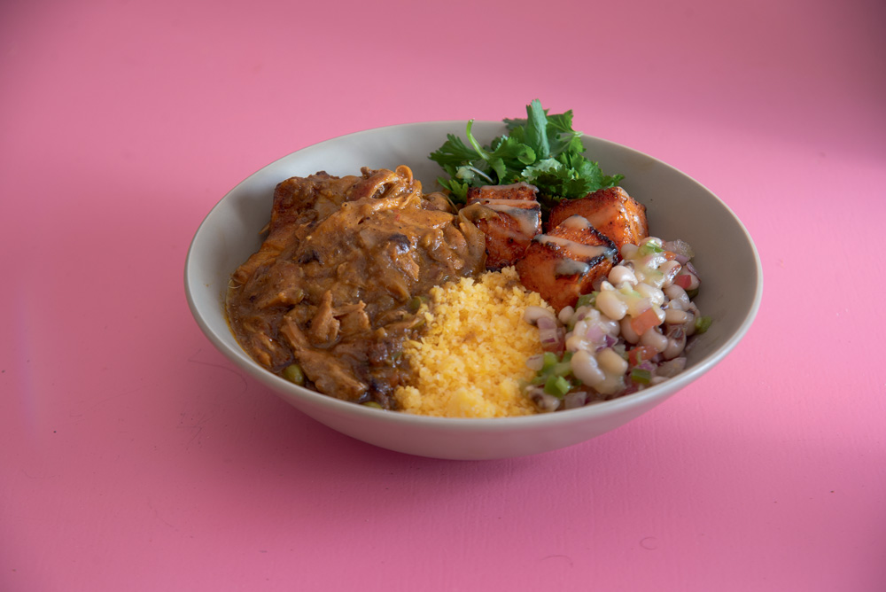 COMER & BEBER 2023 – Cuscuz da Irina Em fundo rosa, cumbuca com cuscuz, carne e salada de feijão.