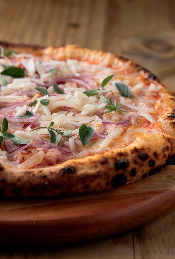 COMER & BEBER 2023 – Carlos Imagem mostra meio pedaço de pizza com faias de cebola e folhinhas verdes por cima.