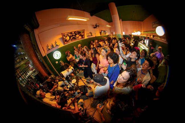 escarcéu No canto esquerdo da imagem, roda de samba e, no resto da foto, bar até o fundo, lotado