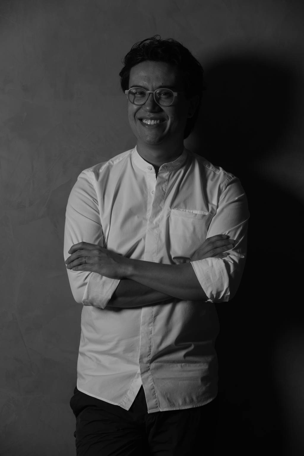 Rodrigo Ohtake (Leo Faria-Divulgação) (1) Foto em preto e branco de homem com traços levemente asiáticos, com camiseta longa branca, de braços cruzados.