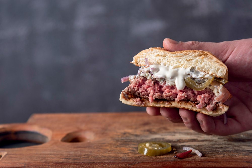 COMER & BEBER 2023 – Z Deli Sandwiches Hambúrguer cortado no meio mostra as camadas de pão, carne, molho e cebola.