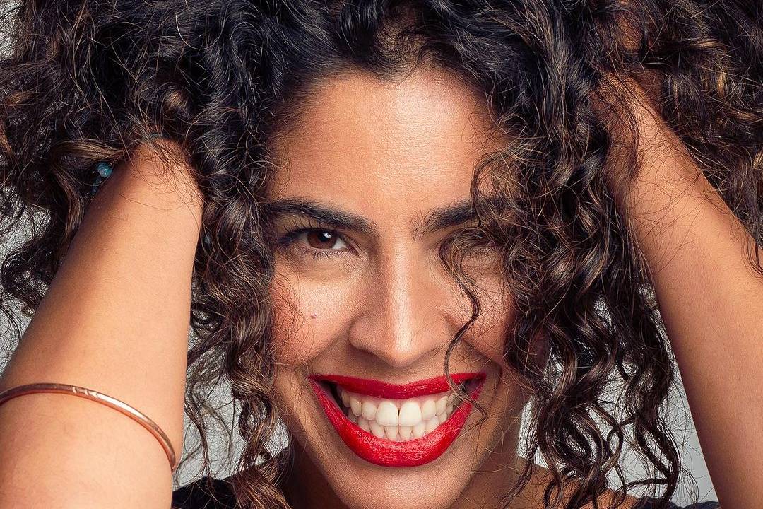 uma mulher de pele negra clara com longos cabelos enrolados sorrindo