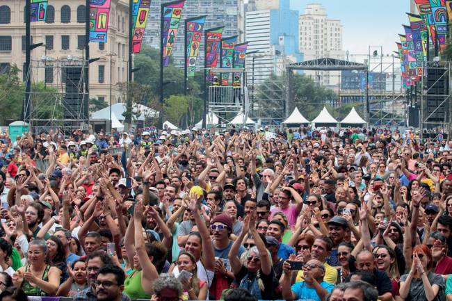 Imagem mostra milhares de pessoas vistas de frente durante show no Vale do Anhangabaú, enorme espaço ao céu aberto, com vários prédios ao fundo e nas laterais da imagem