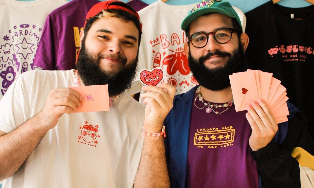 dois homens brancos de barba mostrando pequenos papeis coloridos