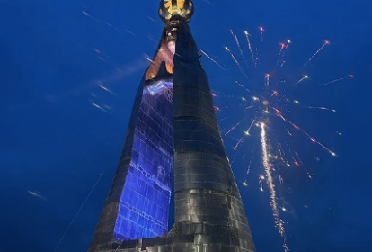 imagem mostra grande estátua de Nossa Senhora, com vão no meio e fogos de artifício no céu no momento da foto