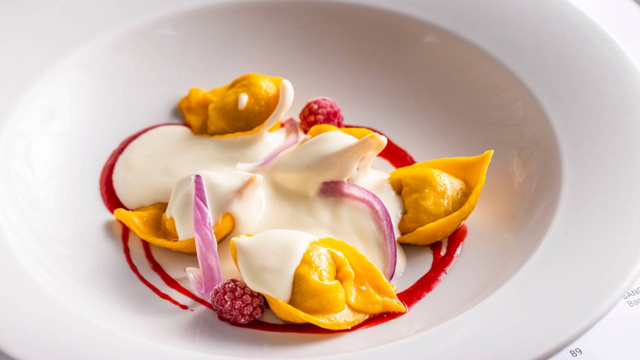 Foto de um prato com massa fresca, creme branco por cima e cebola em fatias.