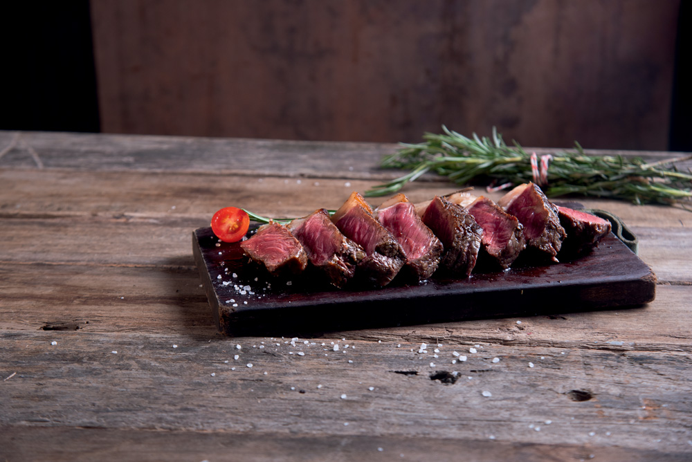 Feira dos Campeões 2023 – Osso Bandeja de madeira com fatias de carne mal passada sobre tampo de madeira