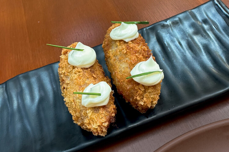 Sobre uma mesa de madeira, dois croquetes com molho branco em cima.