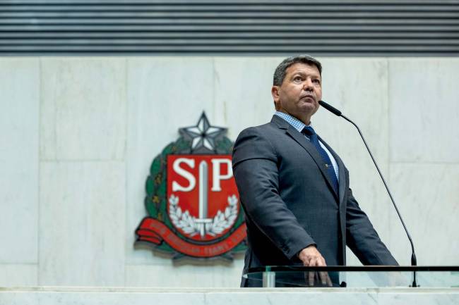 Imagem mostra deputado na tribuna da Assembleia, com logo do estado de São Paulo atrás