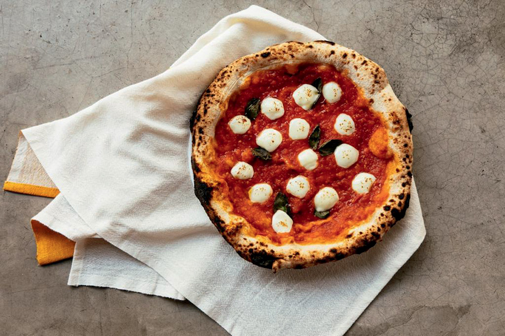 Circuito Comer & Beber – Iza Padaria Artesanal Foto aérea de pizza com molho de tomate e rodelas de muçarela de búfala sobre pano branco
