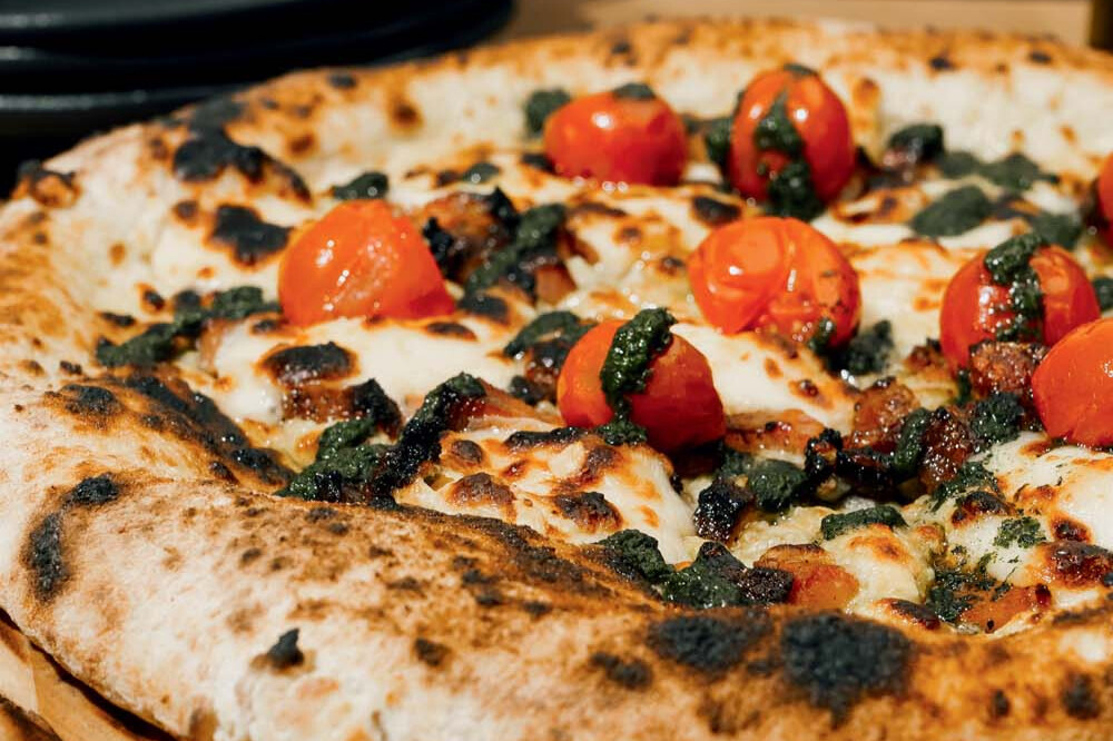 Parte de uma pizza com tomatinhos e queijo por cima.