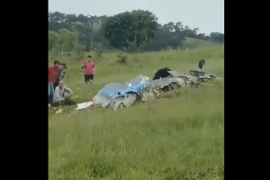 Imagem mostra destroços de avião em área com capim baixo. Cerca de cinco pessoas estão ao redor dos destroços