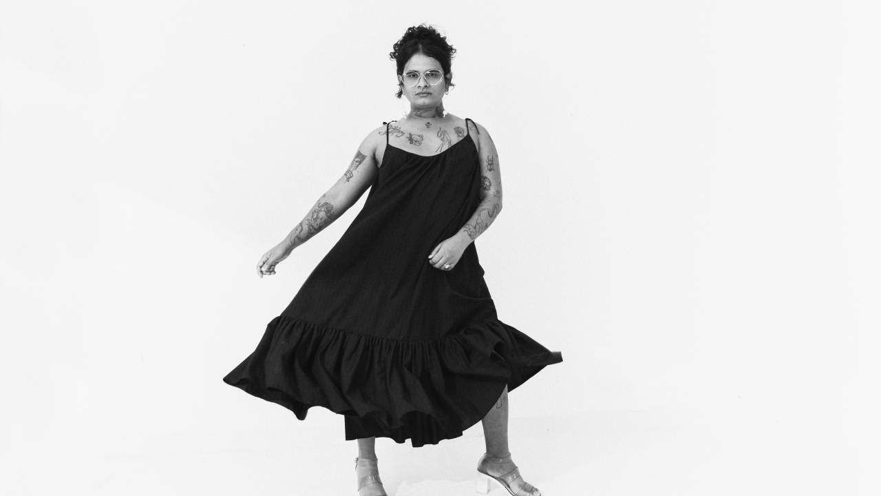Mulher de vestido preto posa dançando em fundo branco