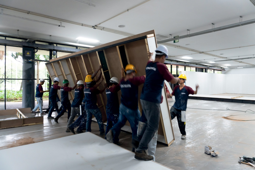 MAS09332.jpg Homens erguem peça grande de madeira no meio de um pavilhão