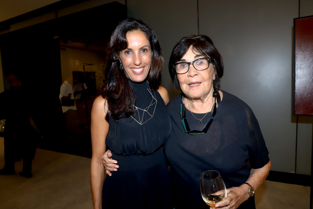 Myra e Raquel Arnaud Crédito Denise Andrade Divulgação.jpg Duas mulheres sorriem, ambas vestindo peças pretas, a da esquerda com cabelos longos pretos, a da direita curtos