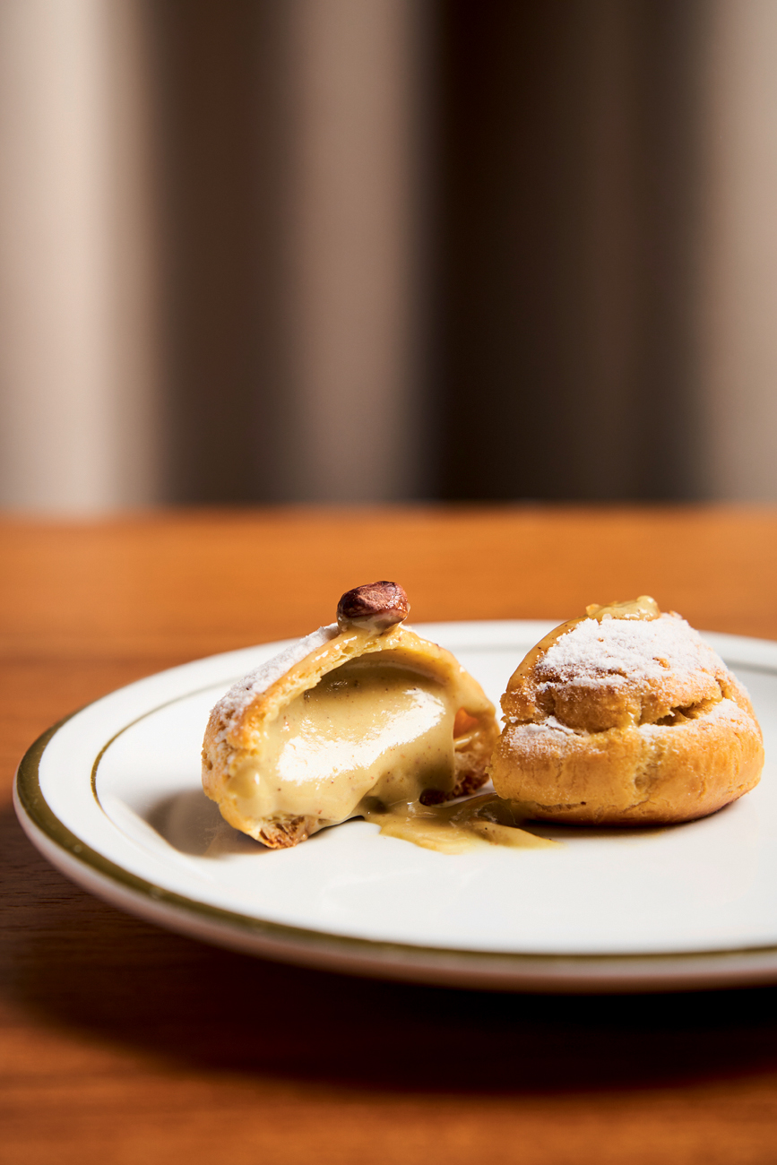 Le Jazz Brasserie Prato de louça branca sobre mesa de madeira com choux cream cortada ao meio com recheio escorrendo