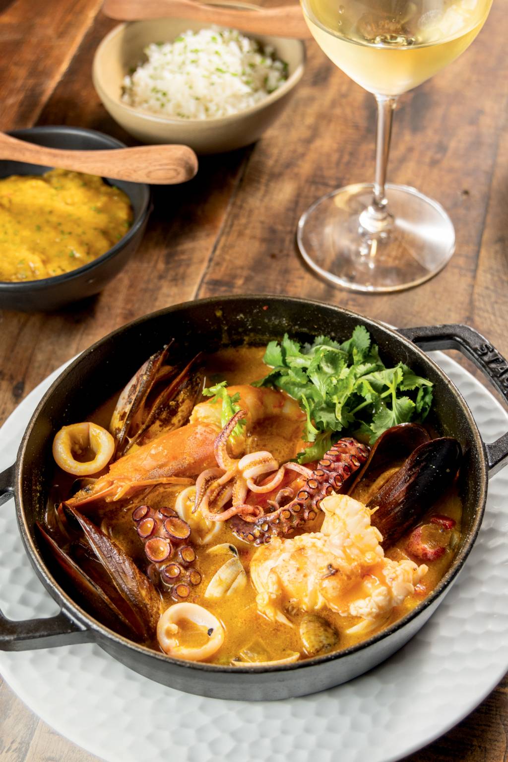Dalva e Dito Panelinha de ferro com moqueca de frutos do mar, tentáculos de polvo e mariscos sobre prato de louça branca